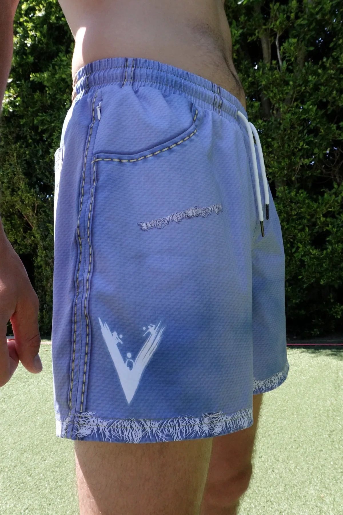 Side on-body fit of JORTS showing the V logo, pockets, stitching, and raw hem